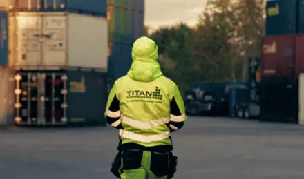 A worker in high-visibility protective clothing standing in a shipping container depot, representing safe handling, logistics operations, and professional container storage solutions.